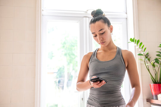 UK, London, Woman in tank top looking at smart phone at home