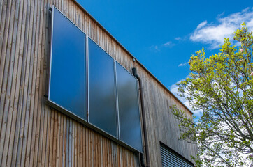 Solar collectors perpendicular to the wooden facade in front of a blue sky