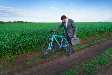 Obraz premium Businessman with a bicycle posing in a green grass field - business concept for freedom, vacation or freelance. Beautiful spring nature.