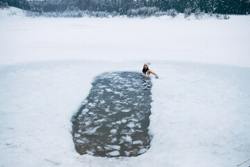 Winter cold swimming. Woman in frozen lake ice hole. Swimmers wellness in icy water. How to swim in cold water. Beautiful young female in zen meditation. Hat and gloves swimming clothes. Nature lake