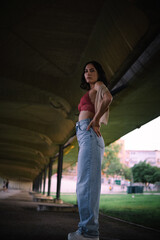 Full body portrait of Caucasian woman. The setting is urban with a symmetrical background with a walkway with pillars on the sides