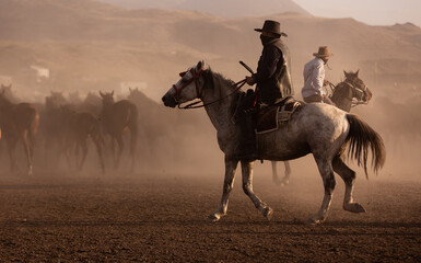 cowboys  next to a herd of horses  