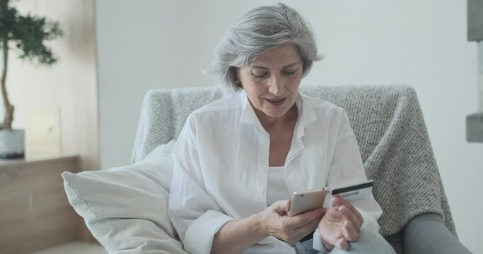Happy mature old female customer holding banking credit card and buying goods. Senior caucasian woman entering credit card numbers for online shopping website and food delivery.