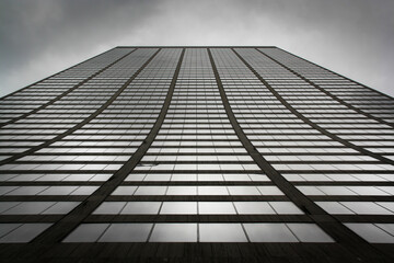 A black and white abstract picture of a skyscraper from right under with sky and clouds showing over the top floor. 