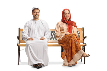 Young man and woman in ethnic clothes sitting on a bench and looking at camera