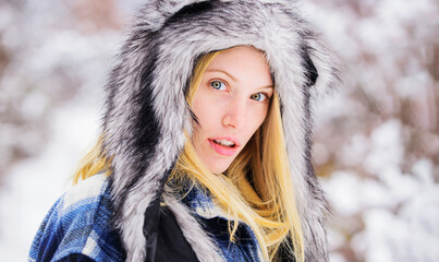 Wintertime. Closeup portrait girl in snow park. Beautiful young woman in warm coat and fur hat....