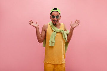 Medium shot of young man with raised shoulders and palms at his sides, posing over pink wall in...