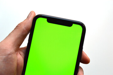Photo of a hand holding a mobile device - iPhone template with green screen to add a customized image or text with chroma key - Smartphone blank screen to show an app, game or website on display