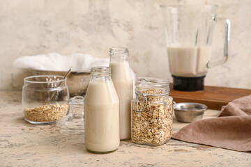 Bottles with tasty oat milk and ingredients on kitchen table