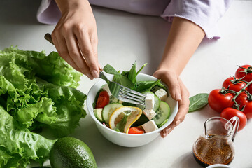 Woman eating healthy salad on table in kitchen