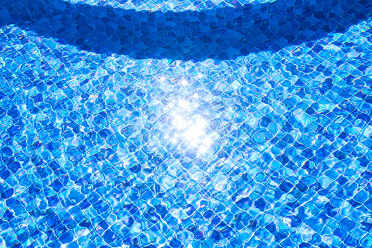Piscina de vinil em uma resid&ecirc;ncia com estampa de mosaico quadriculado em diversos tons de cor azul. Piscina com degraus internos e reflexo da luz do sol brilhando na &aacute;gua.
