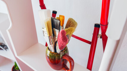 Close-up of a set of colorful brushes in a brown vasel in a bright and white room with natural lighting