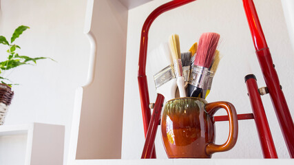 Close-up of a set of colorful brushes in a brown vasel in a bright and white room with natural lighting