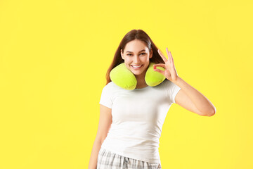 Beautiful young woman with ear plug and travel pillow on yellow background