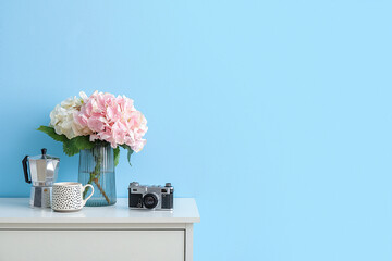 Vase with hydrangea flowers, cup and photo camera on shelf near color wall