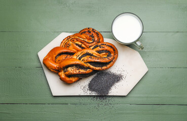 Tasty poppy seed buns with glass of milk on green wooden background