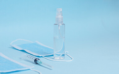
Alcohol in transparent spray dispenser, face mask and syringe with cap. Isolated light blue background. Copy space. Protection and prevention Covid 19, coronavirus.