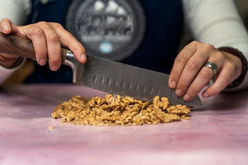 Unrecognizable person using a knife to cut walnuts into small pieces to decorate homemade argentine alfajores