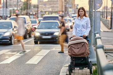 Mother with kid in baby carriage walks near traffic.