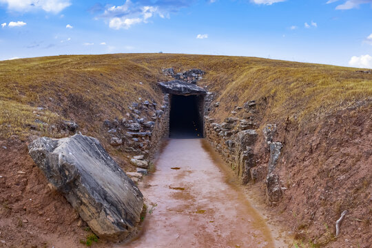 Entrada de un edificio primitivo de piedra oculto en una colina en el paisaje. Dolmen o templo  funerario megal&iacute;tico un d&iacute;a soleado con cielo azul. Oscura entrada de piedra a la tierra.