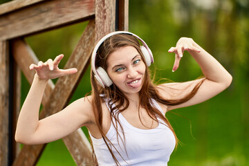 Woman 29 years old in wireless headphones is grimacing in park.