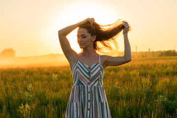 Obraz premium a girl in a dress in a green field in the bright rays of the setting sun.