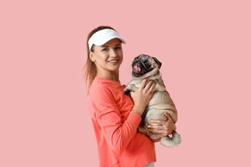 Young woman holding cute pug dog on pink background