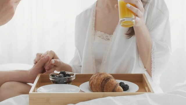 Romantic Couple Having Breakfast And Holding Hands While Relaxing In Bed Together