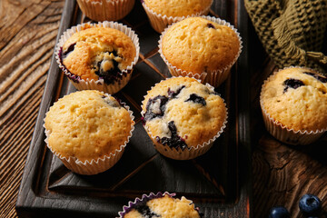 Board with tasty blueberry muffins on wooden background, closeup