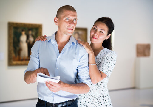 Woman and man walking in picture gallery and looking at exposition