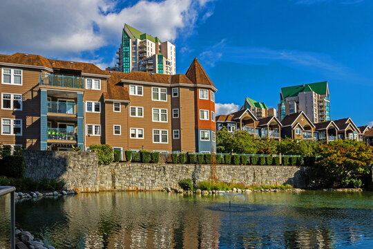 Residential area in the city of Coquitlam, apartment building and townhouses, high-rise buildings in the background and a pond with a fountain in the courtyard of the residential complex