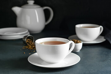 Cups of tasty hojicha green tea on black background