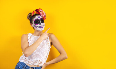 Mexican Catrina, portrait of young latin woman pointing aside on yellow copy space, Halloween party in Mexico