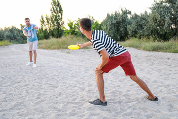 Young men playing frisbee on sea beach