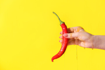 Female hand with chili pepper and honey on color background, closeup