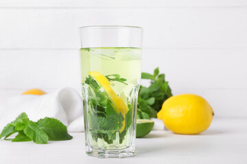 Glass of tasty mint tea with lemon on white wooden background