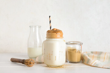 Mason jar of tasty dalgona hojicha latte and chasen on light background