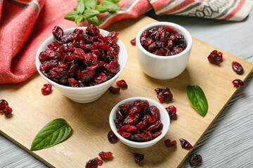 Bowls with tasty dried cranberries on color wooden background, closeup