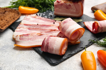 Board with slices of tasty smoked bacon and fresh vegetables on light background