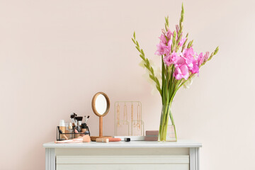 Vase with beautiful gladiolus flowers, female accessories and cosmetics on table against color wall - obrazy, fototapety, plakaty