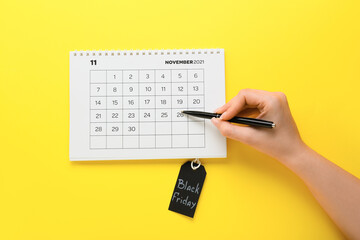 Woman marking date of Black Friday in calendar on color background