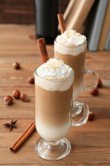 Glass cups of tasty latte with nuts on wooden background