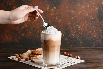 Female hand with glass of tasty latte and nuts on table