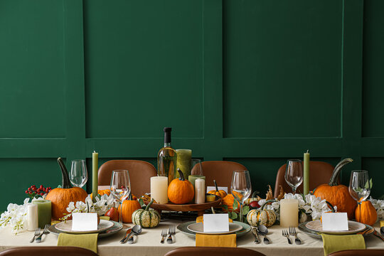 Autumn table setting with fresh pumpkins and flowers near green wall