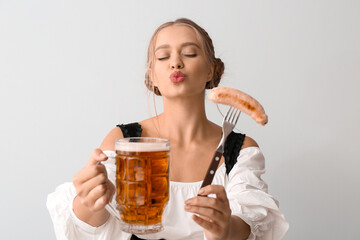 Beautiful woman in traditional German costume, with sausage and mug of beer on grey background