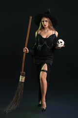 Sexy young witch with skull and broom on dark background