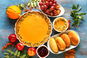 Tasty pumpkin pot pies, buns and fruits for Thanksgiving Day on blue wooden background