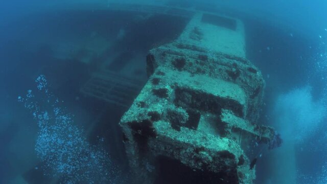 Scuba divers view investigation a large sunken shipwreck deep below the ocean surface