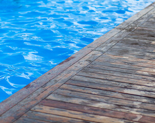 Blue, clear water in an open-air swimming pool. The edges of the pool are made of wood. Water background, ripple and flow with waves. Sea, ocean surface. Overhead top view with place for text.