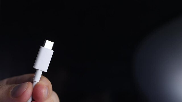 White cable with USB Type-C connector. Connection interface for charge gadget smartphone or laptop, transfer information. Hand on black background